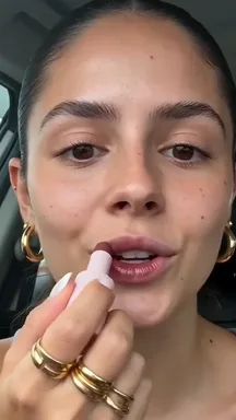A frame from an Adapt video: a woman trying on lipstick in her car.